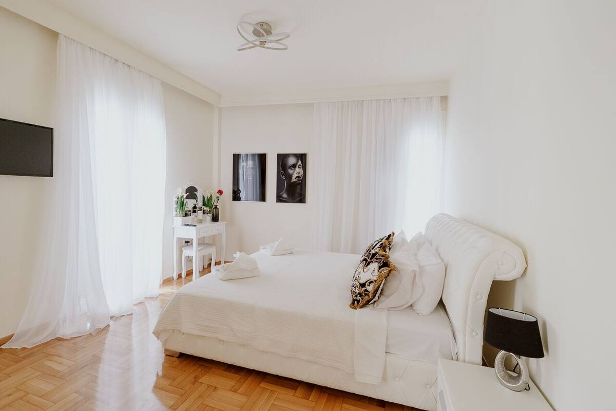 Un dormitorio con una cama grande, una mesita de noche con lámpara, un escritorio con silla y un televisor montado en la pared.