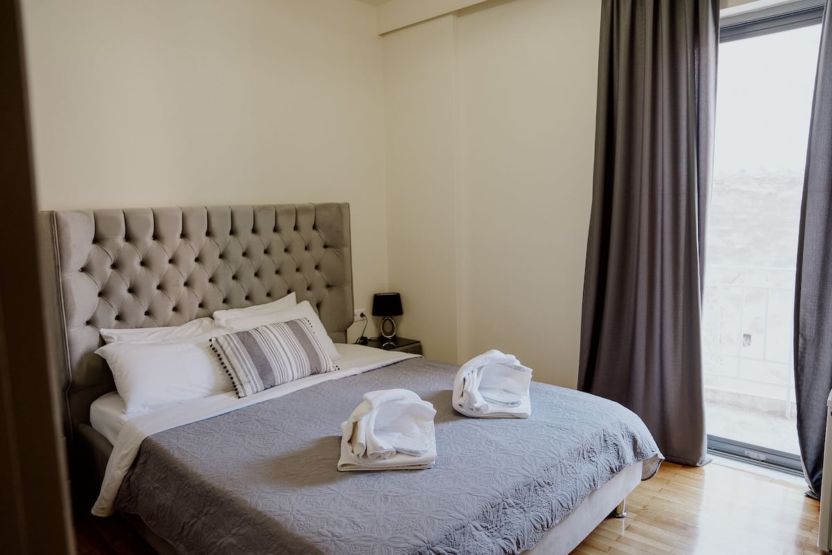 Una cama bien hecha con un cabecero capitonado, un edredón gris y dos toallas dobladas sobre la cama.