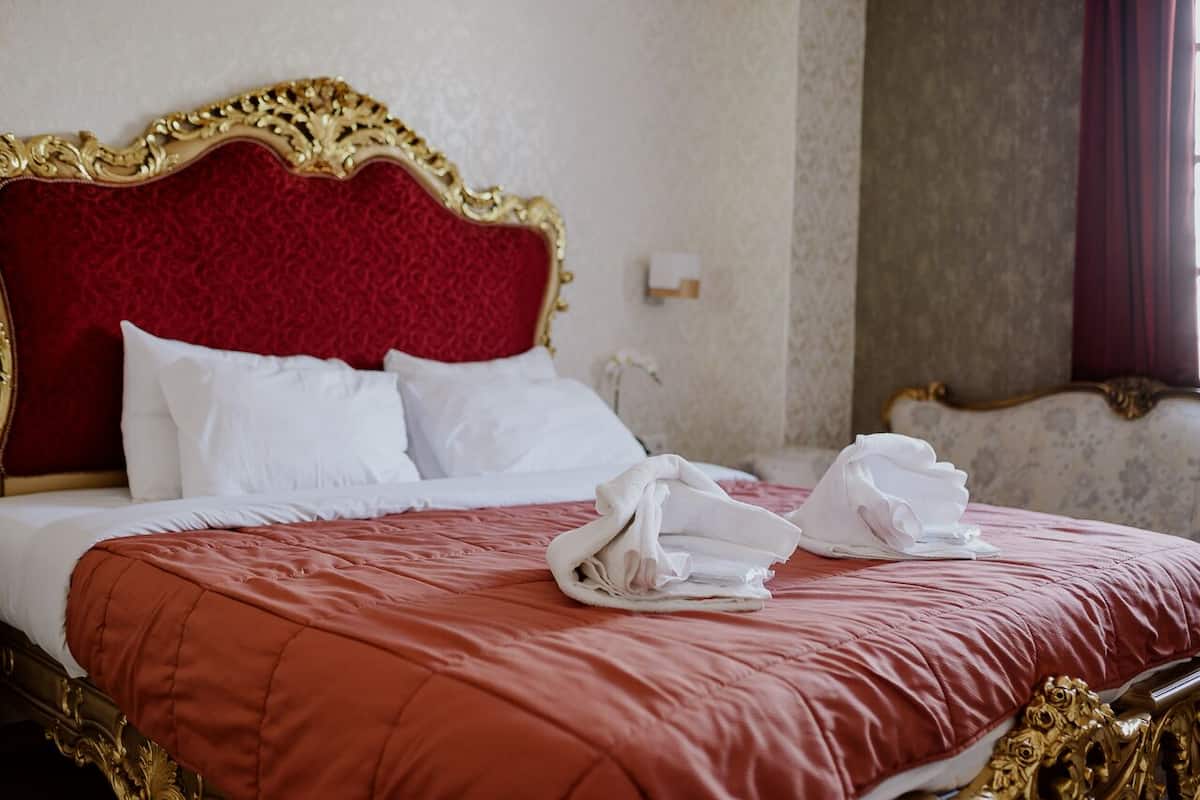 Una cama con colcha roja, almohadas blancas y un cabecero dorado.