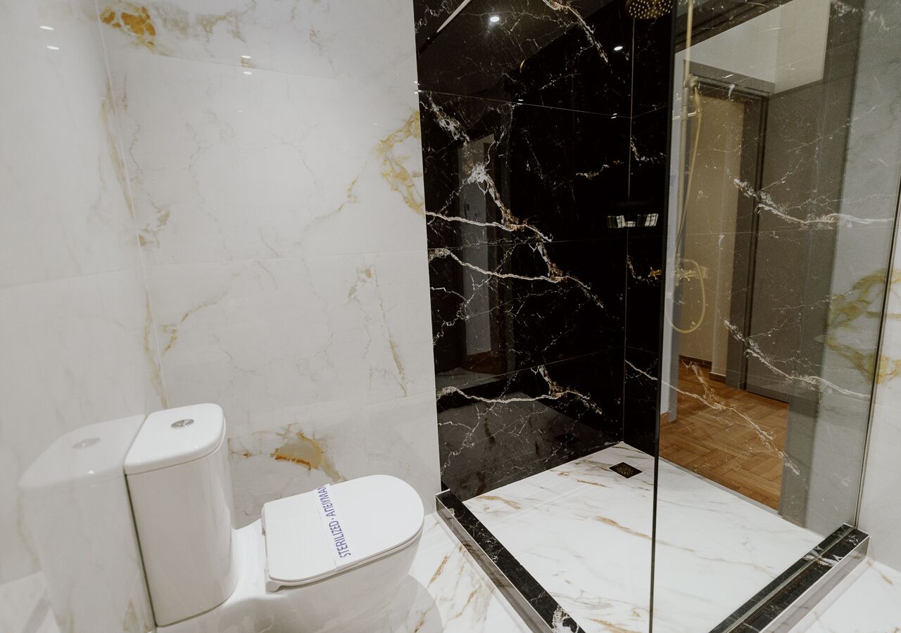 A modern bathroom with a toilet, a bidet, and a glass shower enclosure.