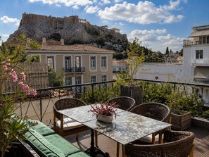 A terrace with wicker furniture, a table, and a view of ancient ruins. - ROH Suites (Athens)