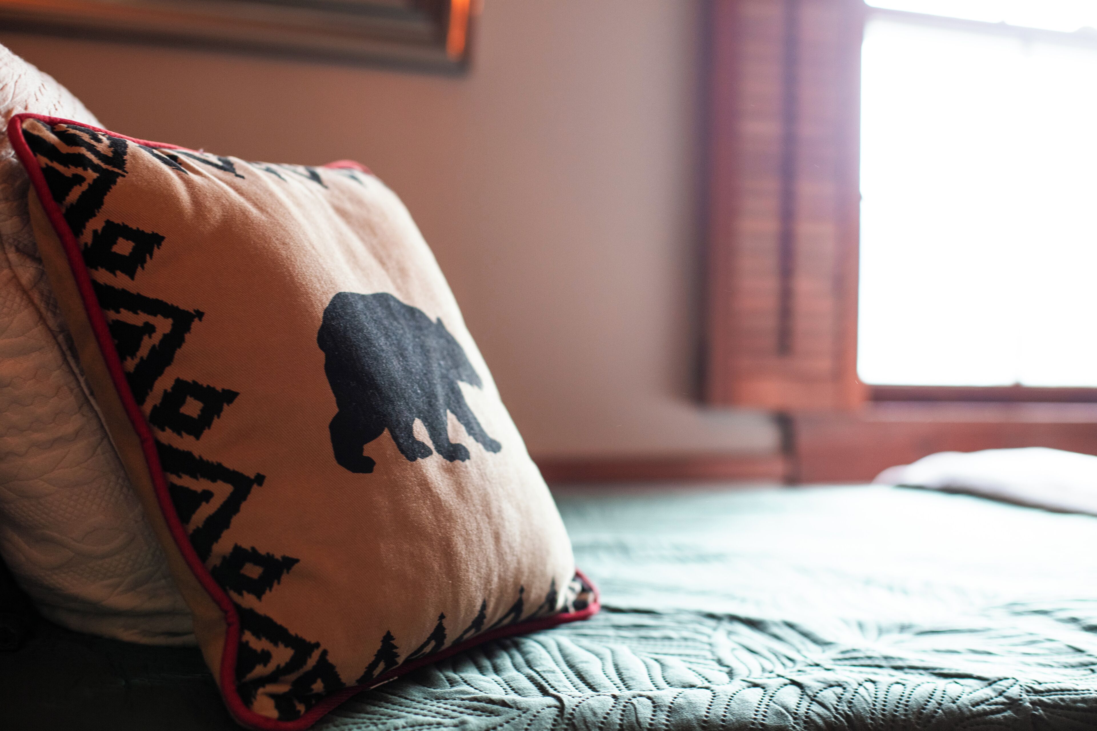 Un letto con una coperta verde trapuntata e un cuscino con la sagoma di un animale nero.