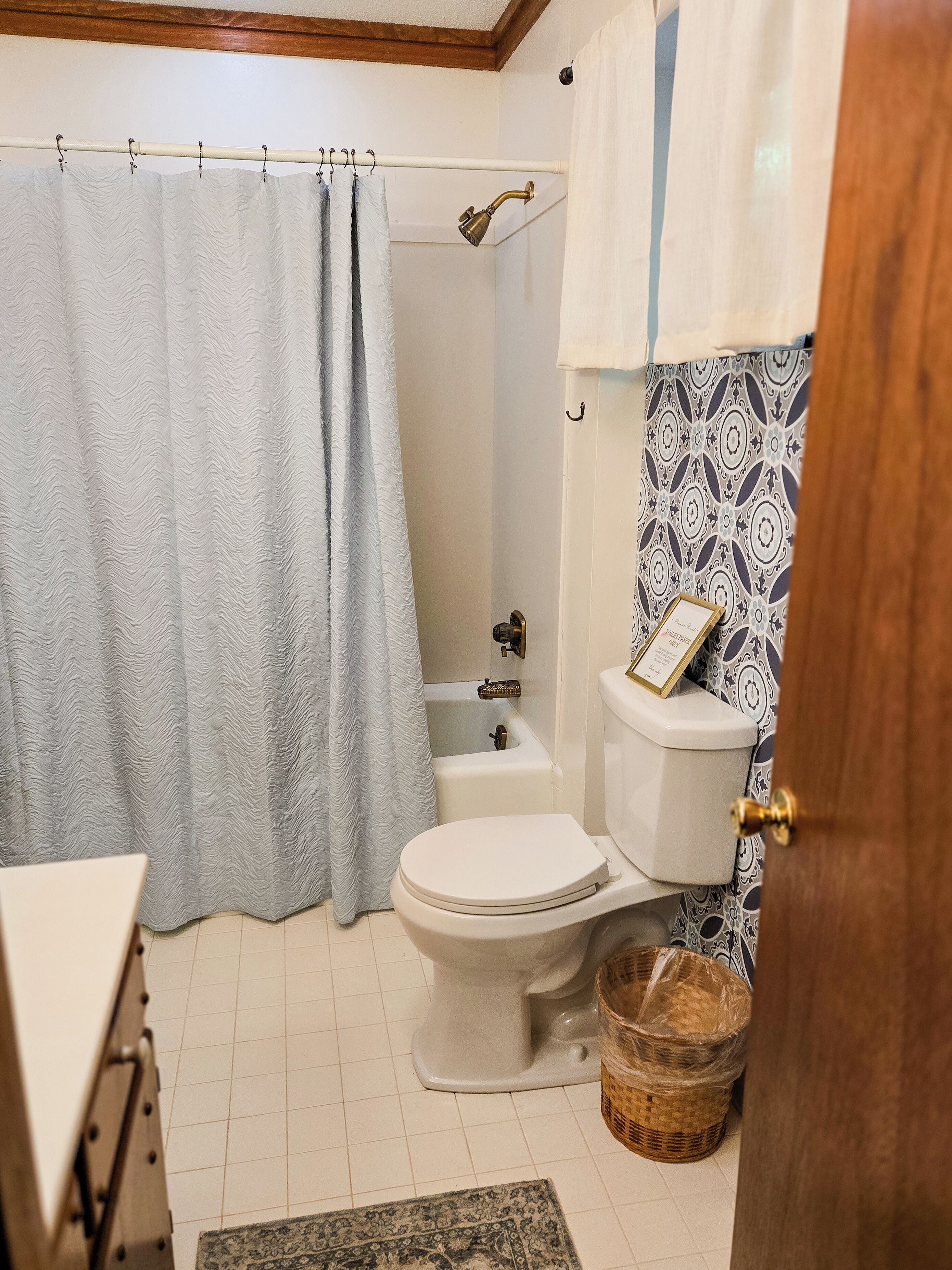 A bathroom with a shower curtain, a toilet, a bathtub, and a patterned wall.