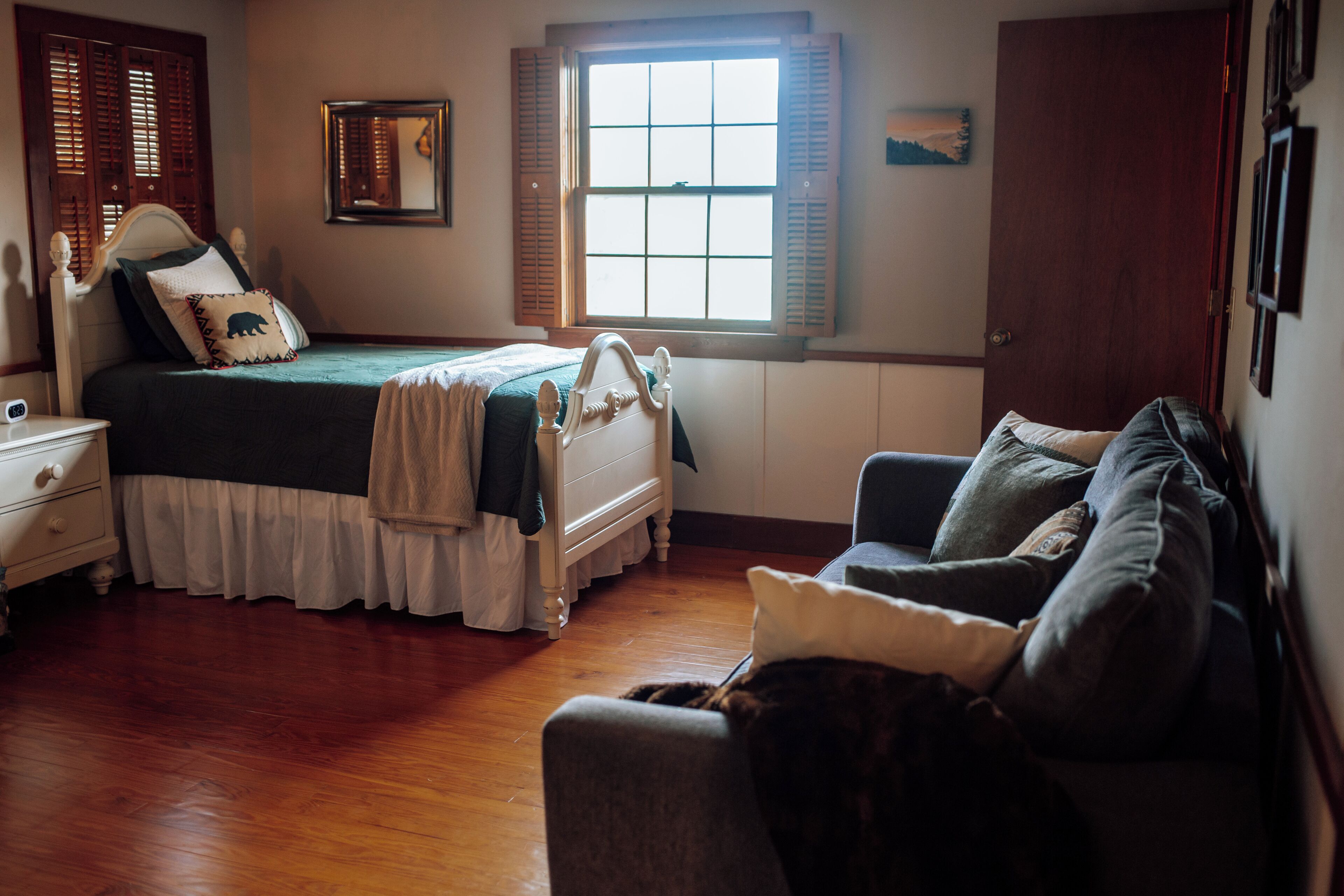 A bedroom with a bed, a chair, a nightstand, a window, and a door.