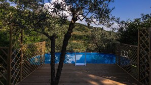 Una terraza de madera que da a una piscina rodeada de árboles.