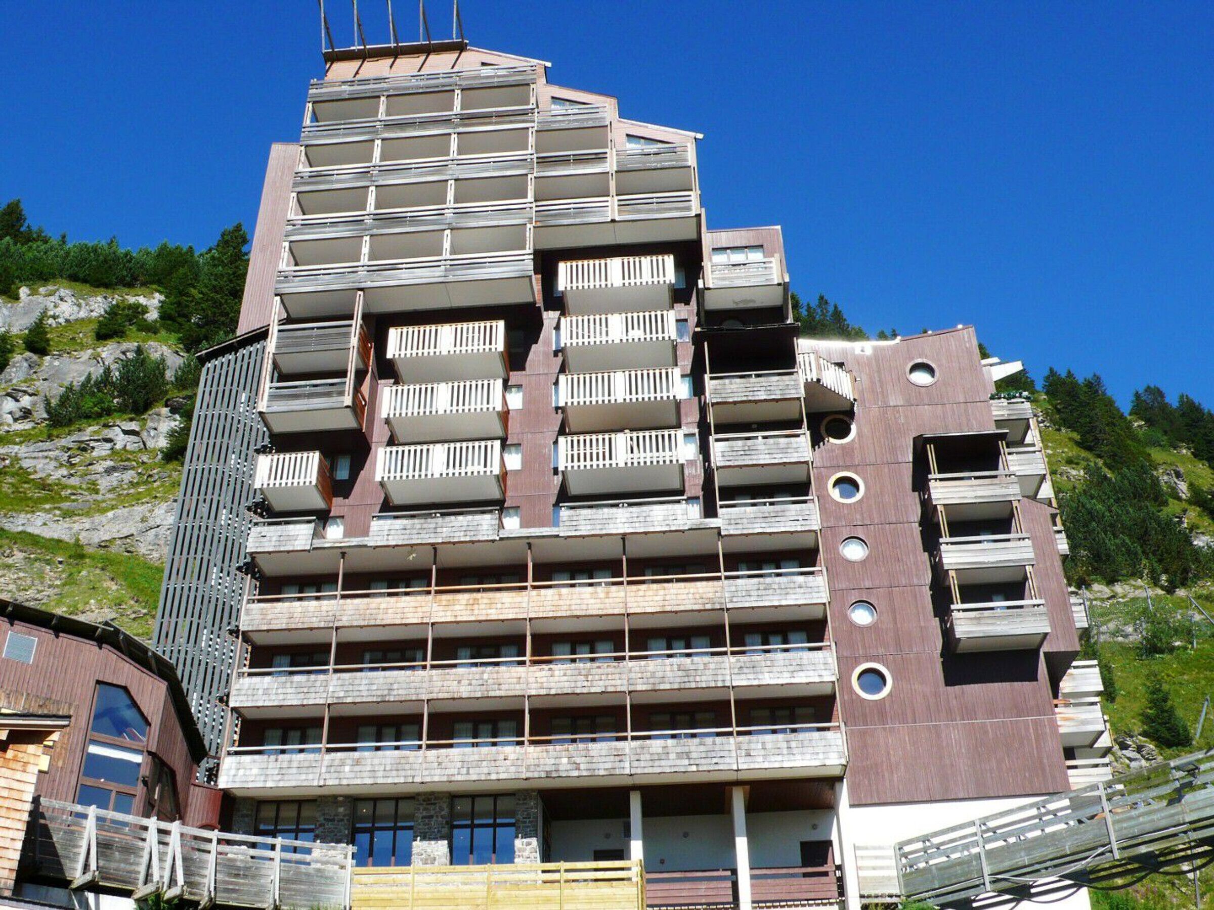 A multi-story building with balconies, a wooden facade, and a mountainous backdrop.