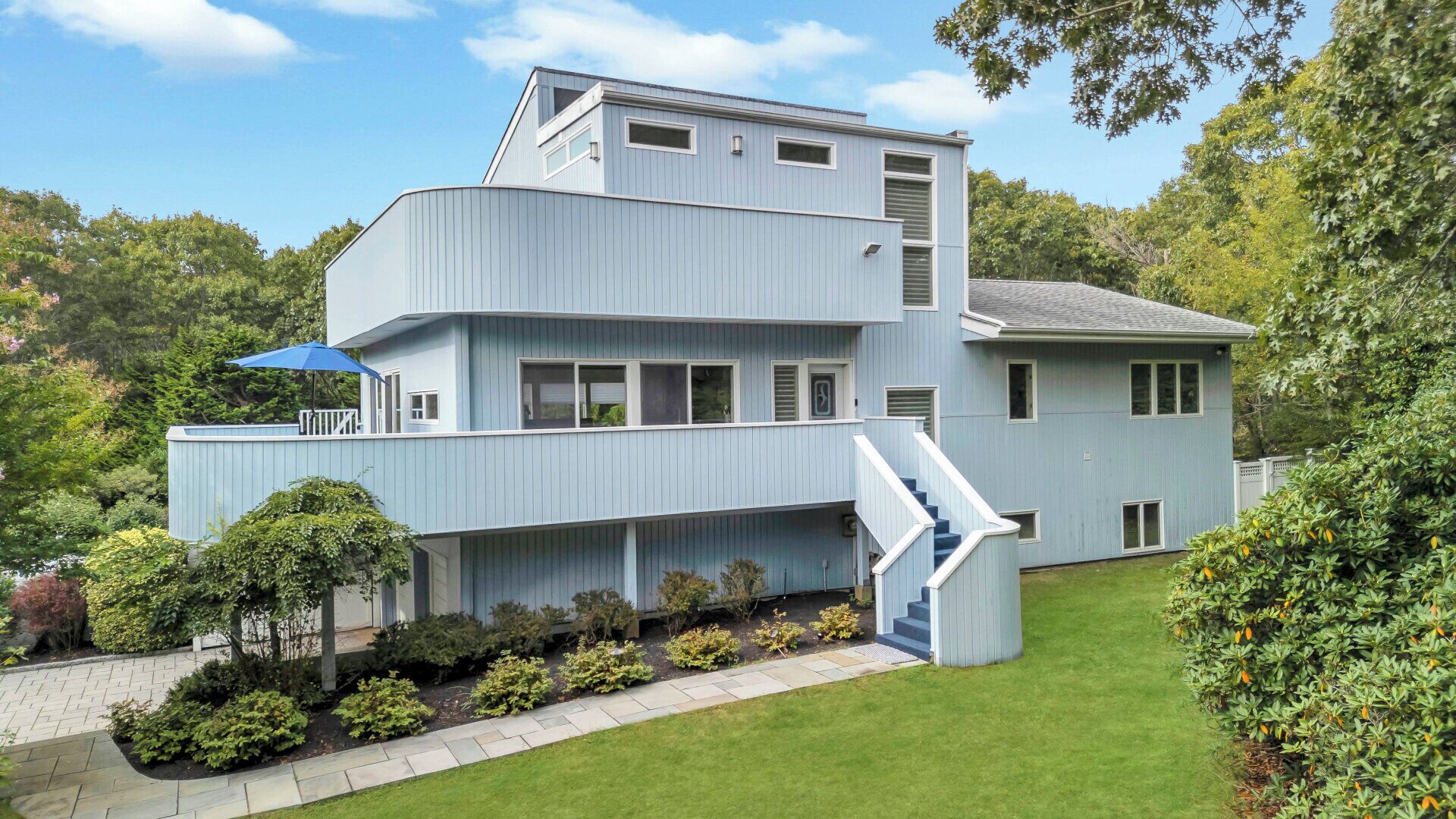 A modern two-story house with a flat roof, a covered porch, and a staircase leading to the upper level.