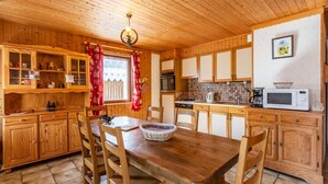 Eine Holzhütte mit einer Küche, einem Esstisch, Stühlen, Schränken und einem Fenster mit roten Vorhängen.