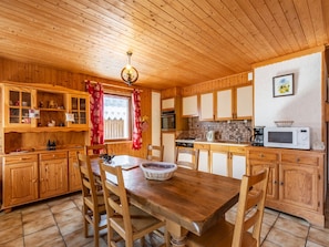 A wooden cabin kitchen with a dining table, chairs, cabinets, and a window with red curtains.