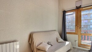 Una habitación con sofá color beige, alfombra mullida, radiador y ventana con cortinas.