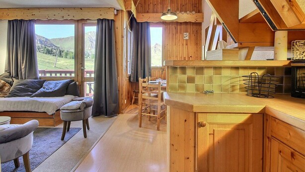 Interior acogedor de una cabaña con comedor de madera, cocina con salpicadero de azulejos y un amplio ventanal con vistas a un paisaje pintoresco.
