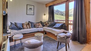 Una habitación acogedora con un amplio ventanal, un sofá, dos otomanas y una mesita.