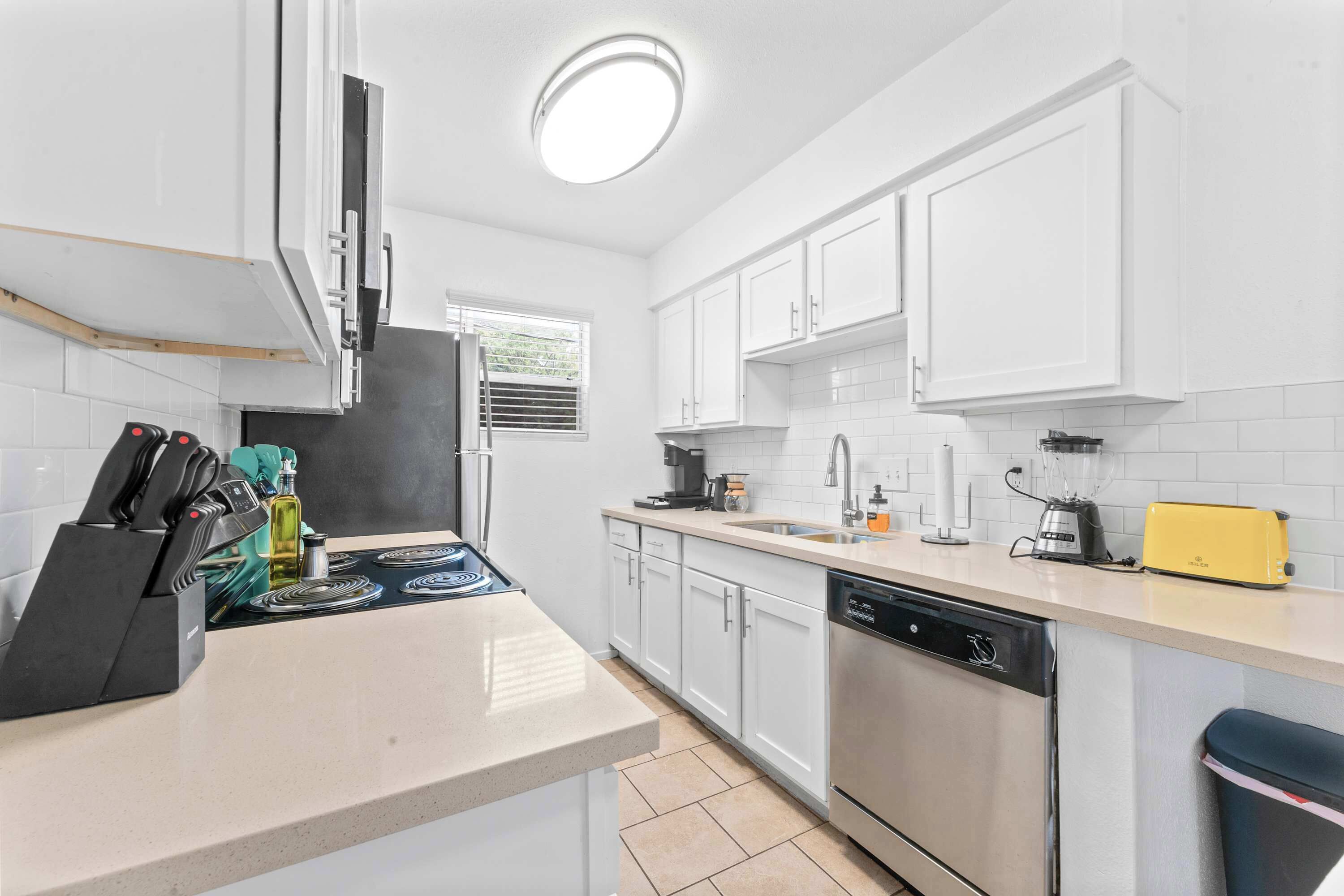 A kitchen with white cabinets, a dishwasher, a stove, and a window.
