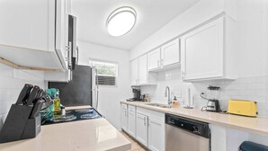 Une cuisine avec des armoires blanches, un lave-vaisselle, une cuisinière et une fenêtre.