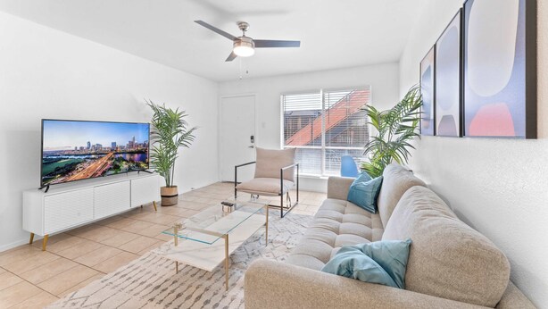 Un salon équipé d’un téléviseur à écran plat, d’un ventilateur de plafond, d’un canapé, d’une table basse et de deux plantes en pot.