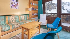 Ett mysigt rum med en soffa och ett bord i trä, en bokhylla och en utsikt över snötäckta berg genom ett stort fönster.