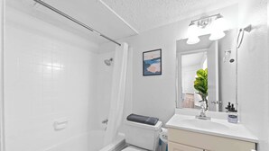 A bathroom with a white bathtub, toilet, and sink. There is a mirror with lights above the sink and a framed picture on the wall. - Central Hyde Park studio close to UT, Moody Center (Austin)