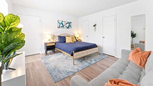 A bedroom with a bed, bedside tables, a grey sofa, a large plant, and artwork on the walls. - Central Hyde Park studio close to UT, Moody Center (Austin)