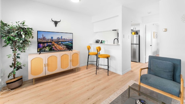Una sala de estar moderna con un televisor de pantalla plana, un sofá, dos sillas amarillas, un mueble de madera y una planta en maceta.