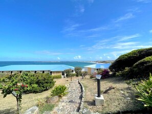 A resort with a clear view of the ocean, a stone pathway, and several buildings with blue roofs.