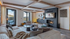 A spacious living room with a large sofa, a fireplace, and a television. - New 86m² in Courchevel 1850 - Ski-in/Ski-out, for 4 adults and 2 kids (Courchevel 1850)
