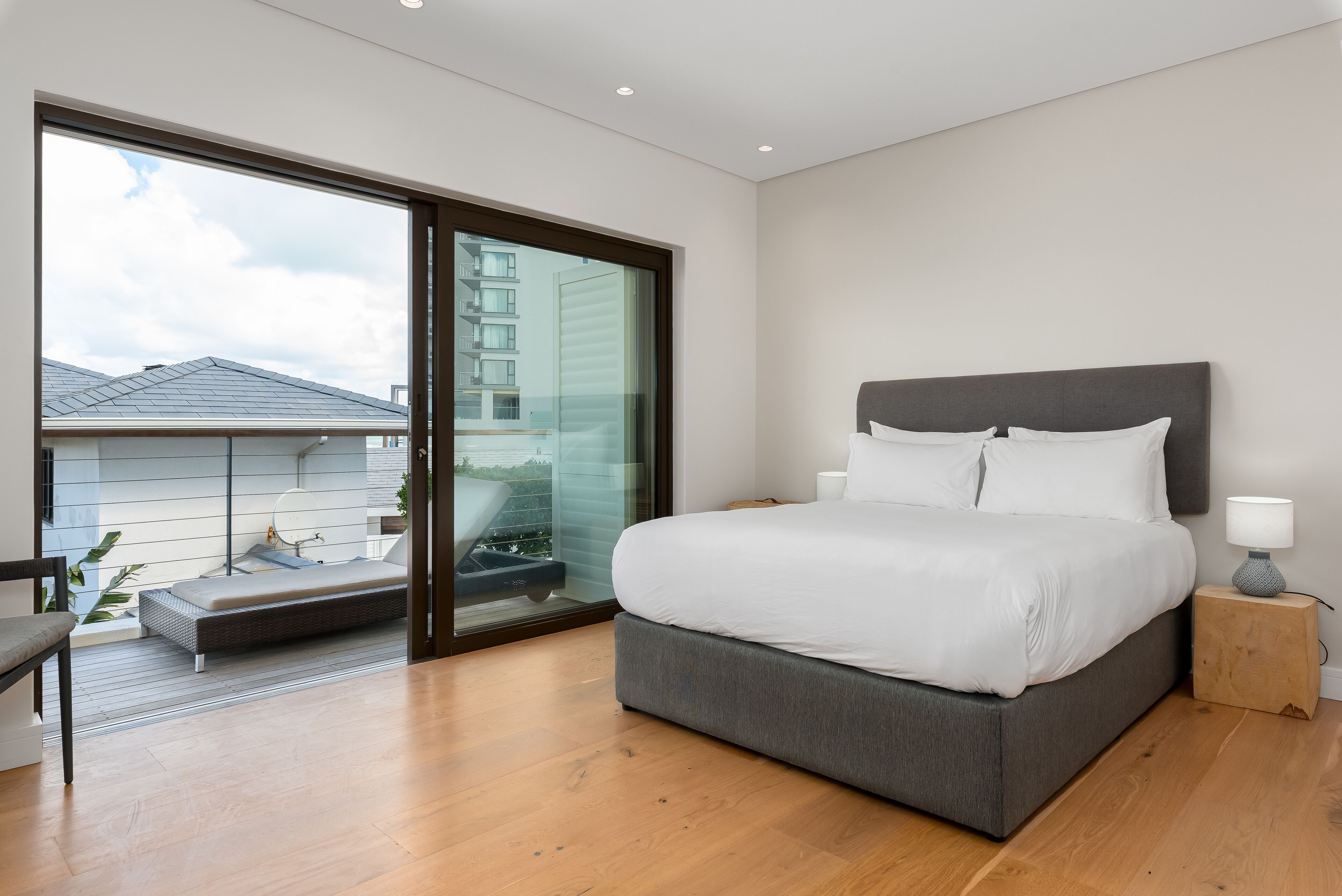 Een moderne slaapkamer met een groot bed, een nachtkastje, een stoel en een glazen schuifdeur naar een balkon.