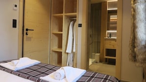 Hotellihuone, jossa on kaksi sänkyä, puinen vaatekaappi, lasinen suihkukaappi ja turkiskoriste.