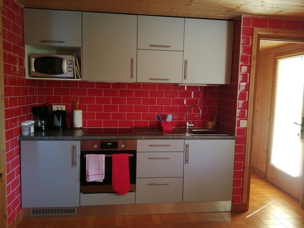 A compact kitchen with red-tiled walls, a microwave, a coffee maker, and a sink.
