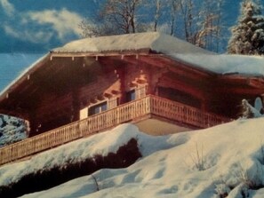 A wooden cabin with a balcony, surrounded by snow-covered trees.