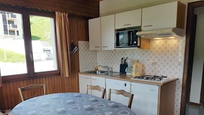 A compact kitchen with a dining table, wooden chairs, a microwave, a stove, and a sink.