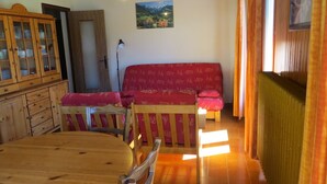 A cozy living room with a wooden dining table, a red sofa with patterned cushions, and a wooden cabinet.