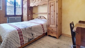 A bedroom with a bed, wooden wardrobe, and a window with a view of trees.
