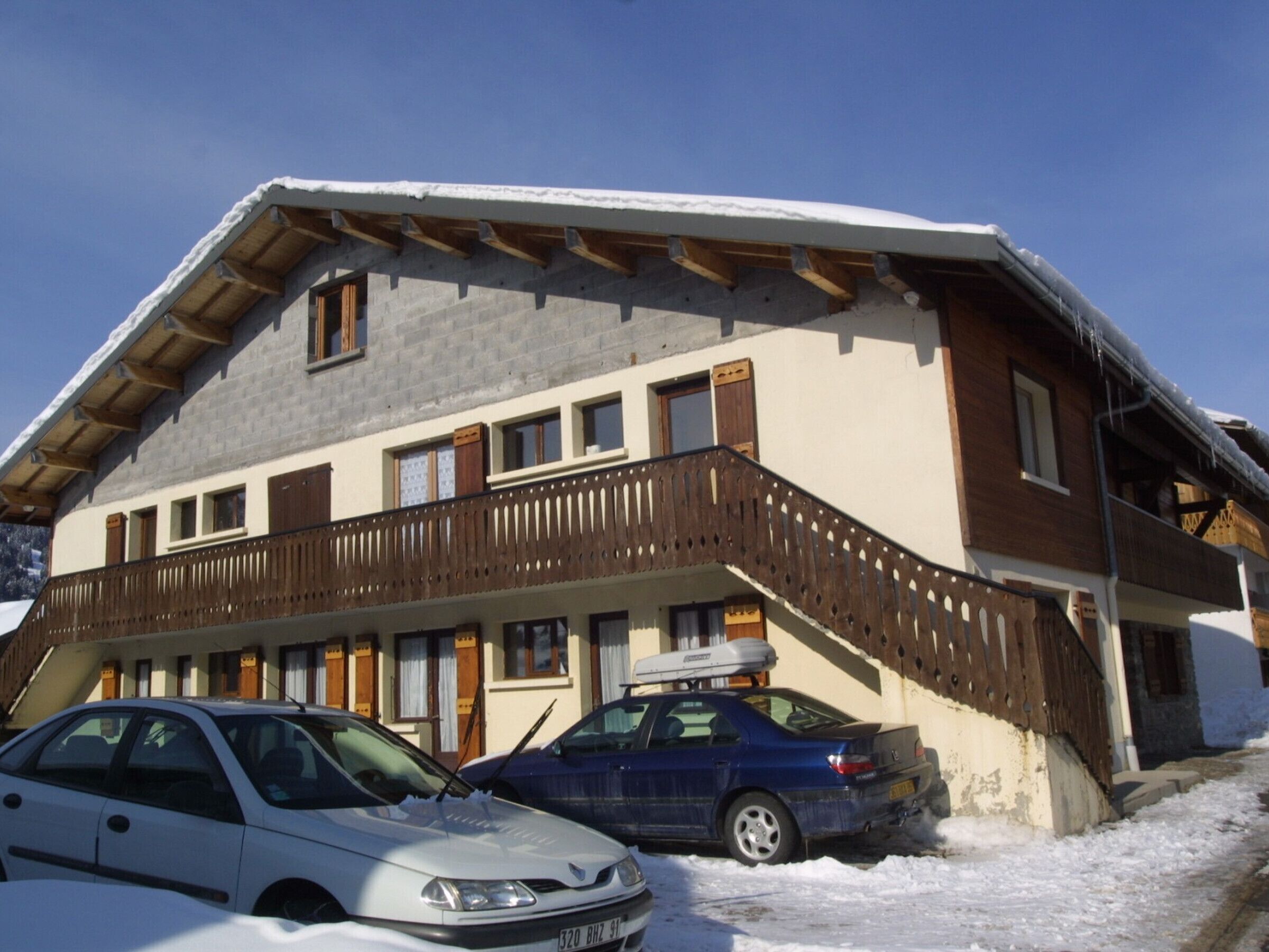 Ein zweistöckiges Gebäude mit einem Holzbalkon und einem geparkten Auto davor.