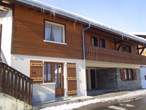 A two-story wooden house with a balcony, a stone foundation, and a snow-covered roof. - Cozy 1BR Apartment for 5 with Balcony, Parking, and Mountain Views near Ski Lifts in Les Gets (Les Gets)