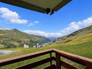 A view from a wooden balcony overlooking a valley with houses, a small church, and a mountain in the background. - Cozy 20m² Studio for 3 with Mountain View Balcony in Reberty 2000, Les Menuires (Les Menuires)