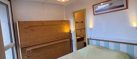 A room with a bed, a wooden cabinet, a framed picture on the wall, and a window.