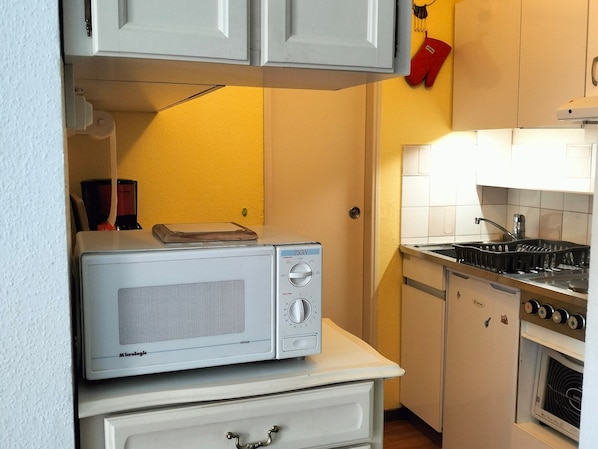 A compact kitchen with a microwave on a counter, a stove, and a sink.