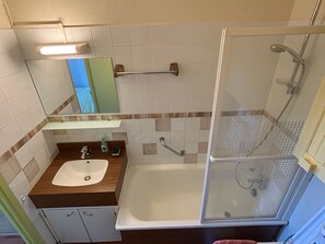 A bathroom with a sink, mirror, towel rack, and a glass-enclosed shower.