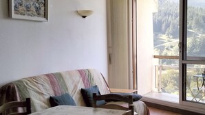 A room with a bed, a table, and a view of a forest through large windows. - T2 Apartment in Balcons de Villard, sleeps 4-6, near slopes (Villard-de-Lans)