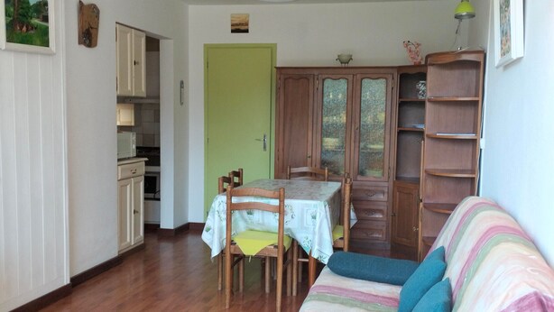 A cozy living room with a wooden dining table, chairs, a sofa with cushions, and a green door. - T2 Apartment in Balcons de Villard, sleeps 4-6, near slopes (Villard-de-Lans)