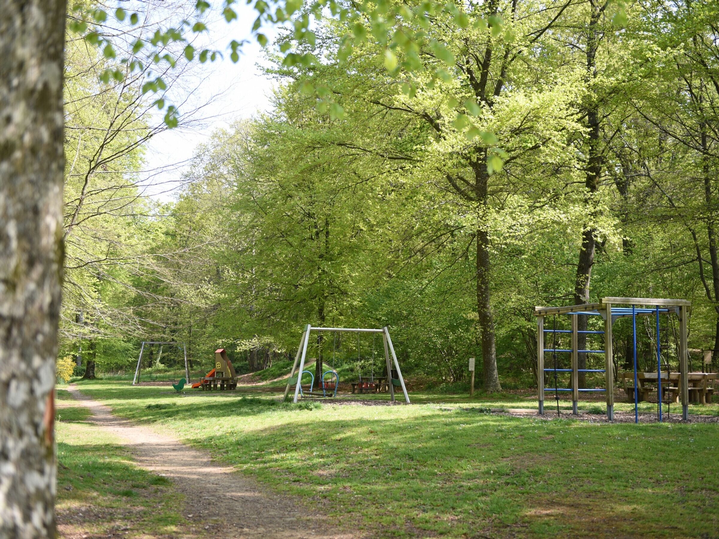 A park with a dirt path, a swing set, and a play structure.