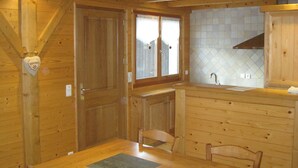 A wooden cabin interior with a dining table, chairs, a kitchen area with a sink, and a window with curtains. - 3 bedrooms, private parking, Wi-Fi, Les Gets (Les Gets)