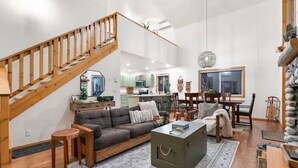 A spacious living area with a wooden staircase, a sofa, a coffee table, and a dining table with chairs. - The Retreat@ the Cottages-tucked in towering pines (McCall)
