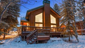 A lodge with a large central window, a covered deck, and a staircase leading to the entrance. - The Retreat@ the Cottages-tucked in towering pines (McCall)