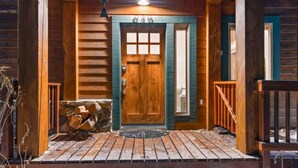 A wooden cabin with a front door, a porch, and a stone wall. - The Retreat@ the Cottages-tucked in towering pines (McCall)