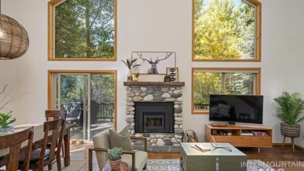 A spacious living room with a stone fireplace, large windows, and a television. - The Retreat@ the Cottages-tucked in towering pines (McCall)