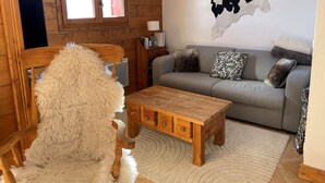A cozy living room with a wooden chair, a grey sofa with patterned cushions, a wooden coffee table, and a large wall-mounted cowhide artwork.
