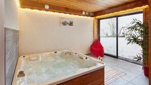 A modern bathroom with a wooden bathtub, a red bean bag, and a potted plant.
