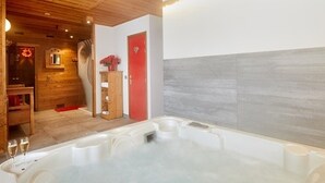 A spa area with a hot tub, wooden flooring, a red door, and a small wooden cabinet with flowers.