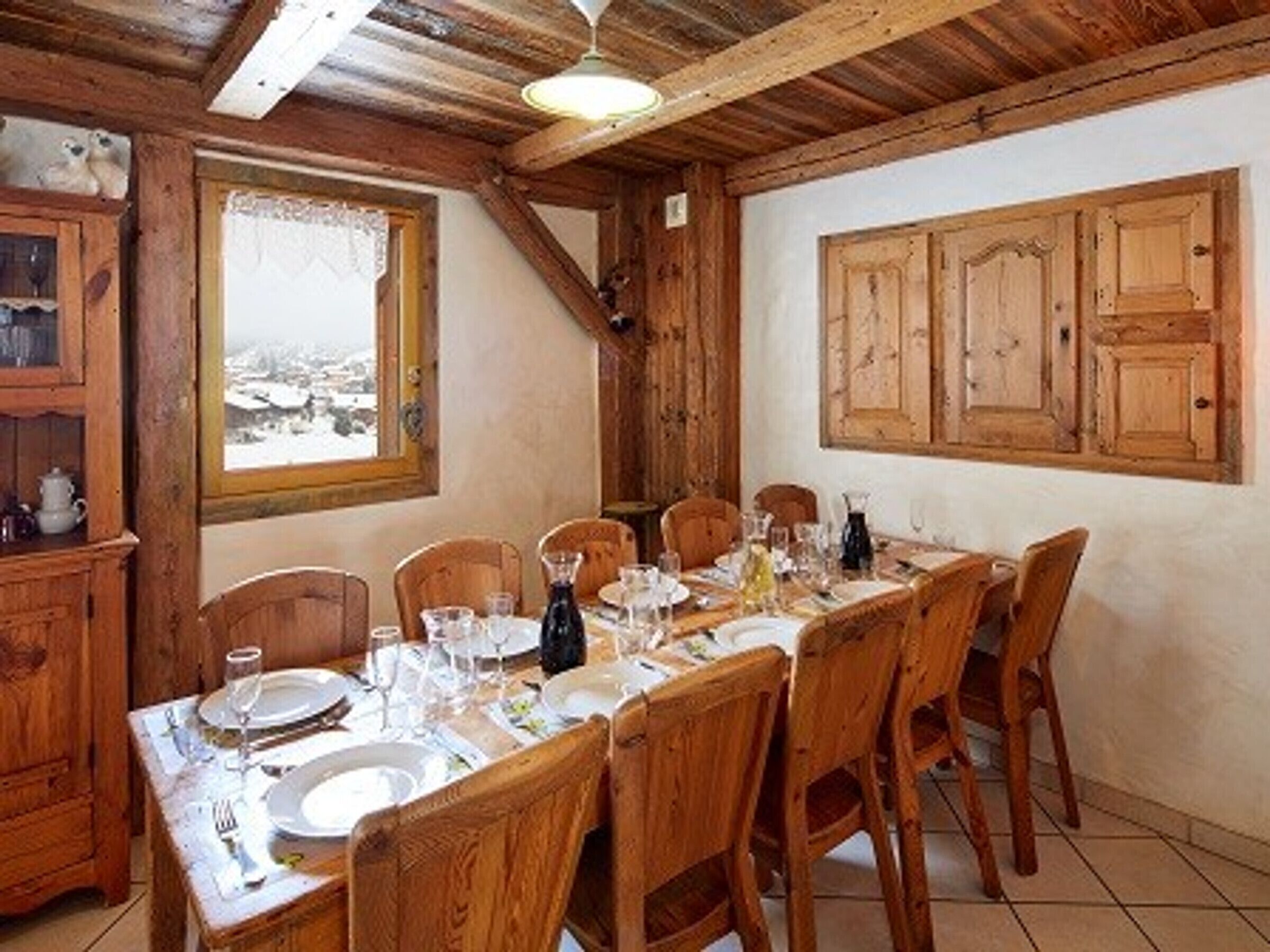 Un comedor con muebles de madera, un ventanal y vista a un paisaje nevado.